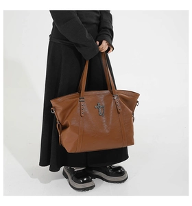 Brown faux leather tote bag with metal cross pendant and rivets shown on a model