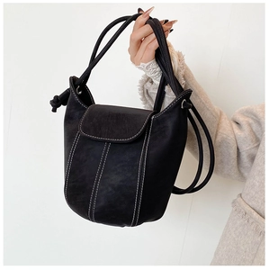 Detail of black matte leather bucket bag with white contrast stitching and drawstring handle