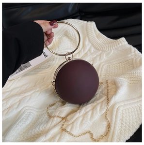 Detail of round burgundy clutch bag with golden ring handle on a cozy knit sweater