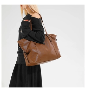 Detail of a large brown leather tote bag showing grainy texture and metallic star studs