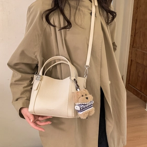 Detail of cream-colored pebble leather bucket bag featuring a cute plush bear charm