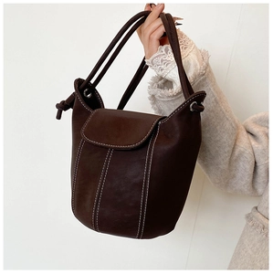 Close-up of a dark brown bucket bag featuring white contrast stitching and tie-knot detail