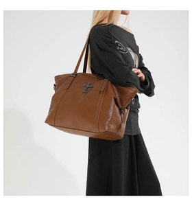 Detail of vintage brown PU leather tote bag with a dark metal cross charm