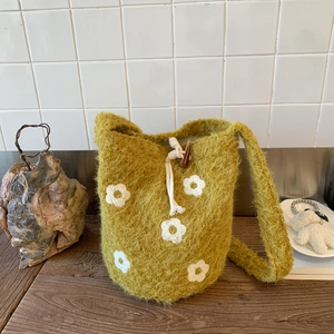 Detail of moss green knitted bucket bag with white crochet flowers and drawstring closure