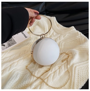 Detail of white spherical evening clutch with golden metal handle on soft sweater