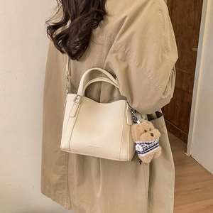 Detail of off-white lychee texture bucket bag with a cute brown teddy bear charm