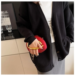 Detail of red hard-shell evening clutch bag with round gold metal handle on a black cardigan