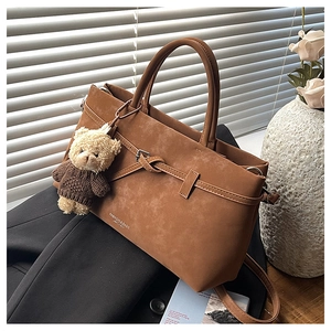 Detail of brown matte tote bag featuring belt buckle and cute teddy bear charm