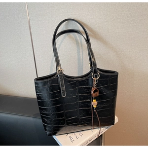Detail shot of black crocodile embossed tote bag with gold logo and tassel charm detail