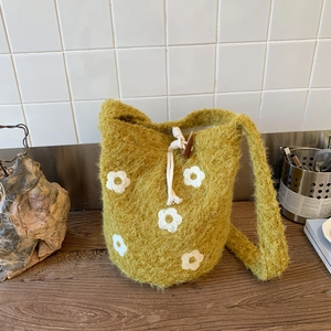 Detail of green knit bucket bag featuring white flower patterns and a toggle closure
