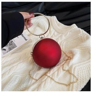 Detailed view of a red spherical clutch bag with a large gold round handle on white fabric