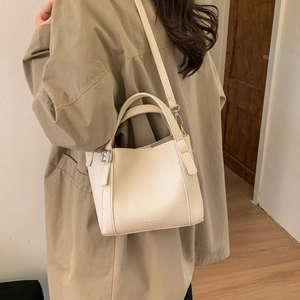 Chic beige lychee textured bucket bag shown with khaki trench coat in indoor lifestyle setting