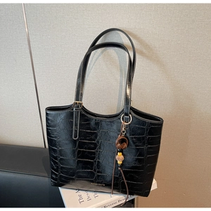Detail of black faux leather tote with crocodile pattern and earphone charm detail