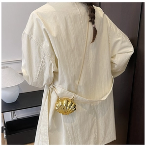 Detail view of a gold shell-shaped mini chain bag worn over a beige trench coat
