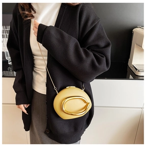 Detail of yellow pebble-shaped crossbody bag with large gold C-accent and slim chain strap