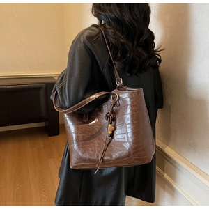 Close-up of a dark brown crocodile texture tote bag with a decorative beaded tassel charm