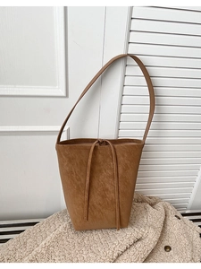Détail du sac seau en cuir marron avec cordon de serrage sur fond texturé blanc