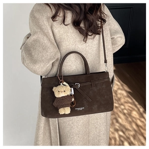 Detailed view of brown suede handbag with bear charm on a beige cashmere coat