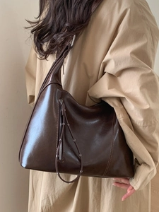 Luxurious dark brown large capacity tote bag in glossy leather worn with khaki trench coat