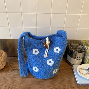 Detailed close-up of blue plush knit bucket bag featuring white floral patterns and wood button