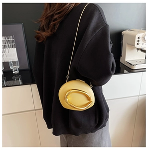 Detail of a beige acrylic box clutch with a bold gold circular metal link and chain strap