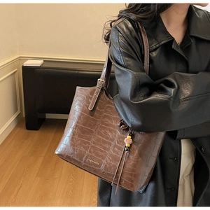 Close-up of brown crocodile texture tote bag with long strap and plush ball charm
