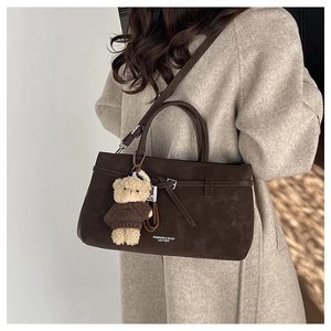 Close-up of dark brown suede handbag with decorative straps and cute bear charm accessory
