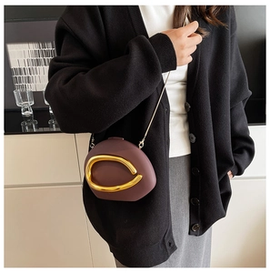 Detail of dark red-brown acrylic clutch bag with streamlined gold metal decor and chain