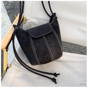 Detail of black leather bucket bag featuring white contrast stitching and drawstring straps