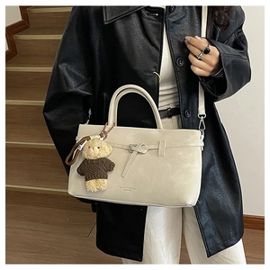Detailed macro view of beige crossbody bag with textured leather and plush bear charm