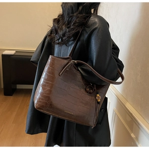 Detail of dark brown faux crocodile leather tote bag with gold logo and charm accessory