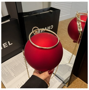 Detail of red spherical evening clutch with gold ring handle and metal chain strap