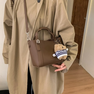 Detail of dark brown leather bucket bag with cute bear pendant and silver hardware