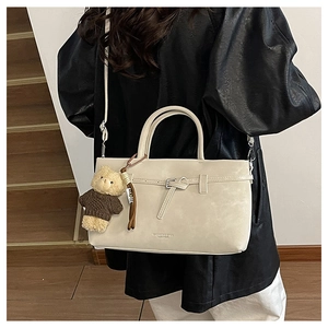 Detail of cream crossbody bag featuring a metal buckle and a cute brown plush bear charm
