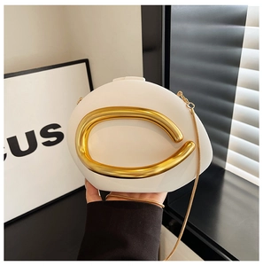 Detail of a creamy white acrylic clutch with a large gold ring handle and metal chain