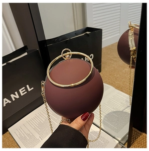 Close-up of matte burgundy sphere evening bag with golden ring handle and chain strap