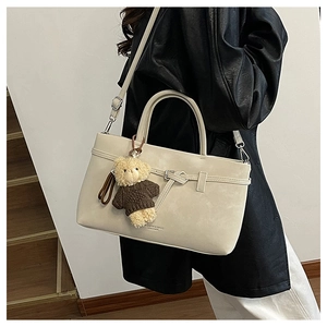 Detail view of cream crossbody bag with teddy bear charm worn with black leather jacket