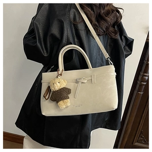 Close-up of cream leather handbag with decorative straps and cute bear keychain charm