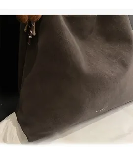 Close-up of dark brown tote bag texture with letter embossing and plush bear charm