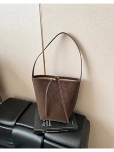Détail d'un cabas en daim café avec fermeture à cordon sur un tabouret en cuir