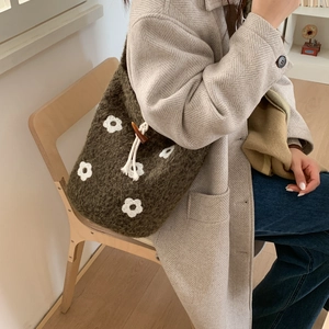 Detail of dark green knit tote bag featuring white floral accents and toggle closure