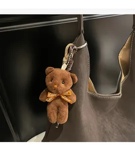 Detailed macro shot of a brown plush bear keychain with a Love ribbon on a tote bag
