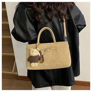 Detail of beige suede tote bag with leather buckle and brown teddy bear charm on model