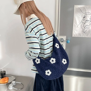 Détail du sac à main bleu marine en peluche avec motifs de fleurs porté par un mannequin