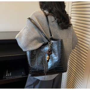 Detail of black crocodile texture tote bag featuring a brand logo and chic tassel charm