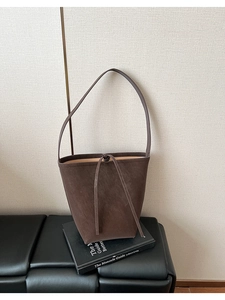 Détail d'un sac seau en daim marron foncé avec de fines bretelles et un nœud décoratif
