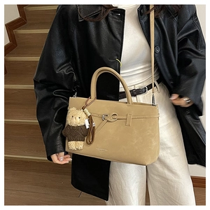 Detail of khaki tote bag with knot decor, bear charm, and textured leather finish