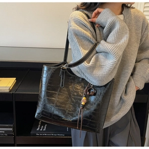 Detail of black crocodile embossed leather tote bag with branded logo and decorative charm