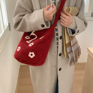Detail of red knitted plush crossbody bag with white flower patterns and drawstring closure
