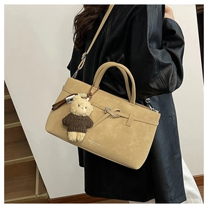 Detail of beige PU leather handbag with decorative metal buckle and plush bear charm